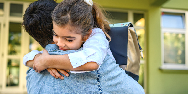 pai abraçando a filha com a mochila de escola nas costas