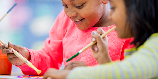 Duas meninas com pincel na mão fazer artes visuais no Colégio Classe A. 