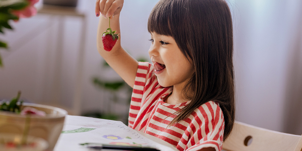 Menina brinca comendo morango e o Colégio Classe A orienta sobre alimentação saudável. 