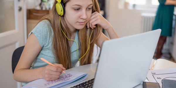 Aluna estuda com fone, caderno e na frente do computador e Colégio Classe A fala dos desafios da educação para a Geração Alpha