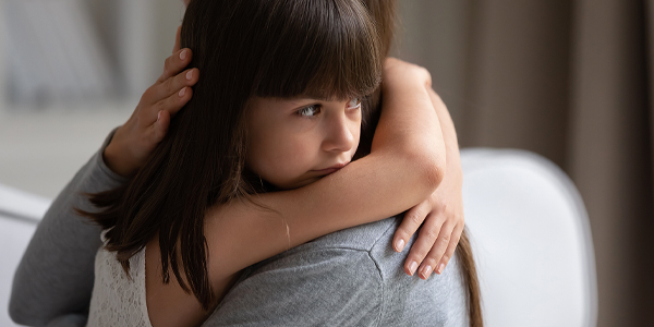 menina com expressão de tristeza recebendo um abraço